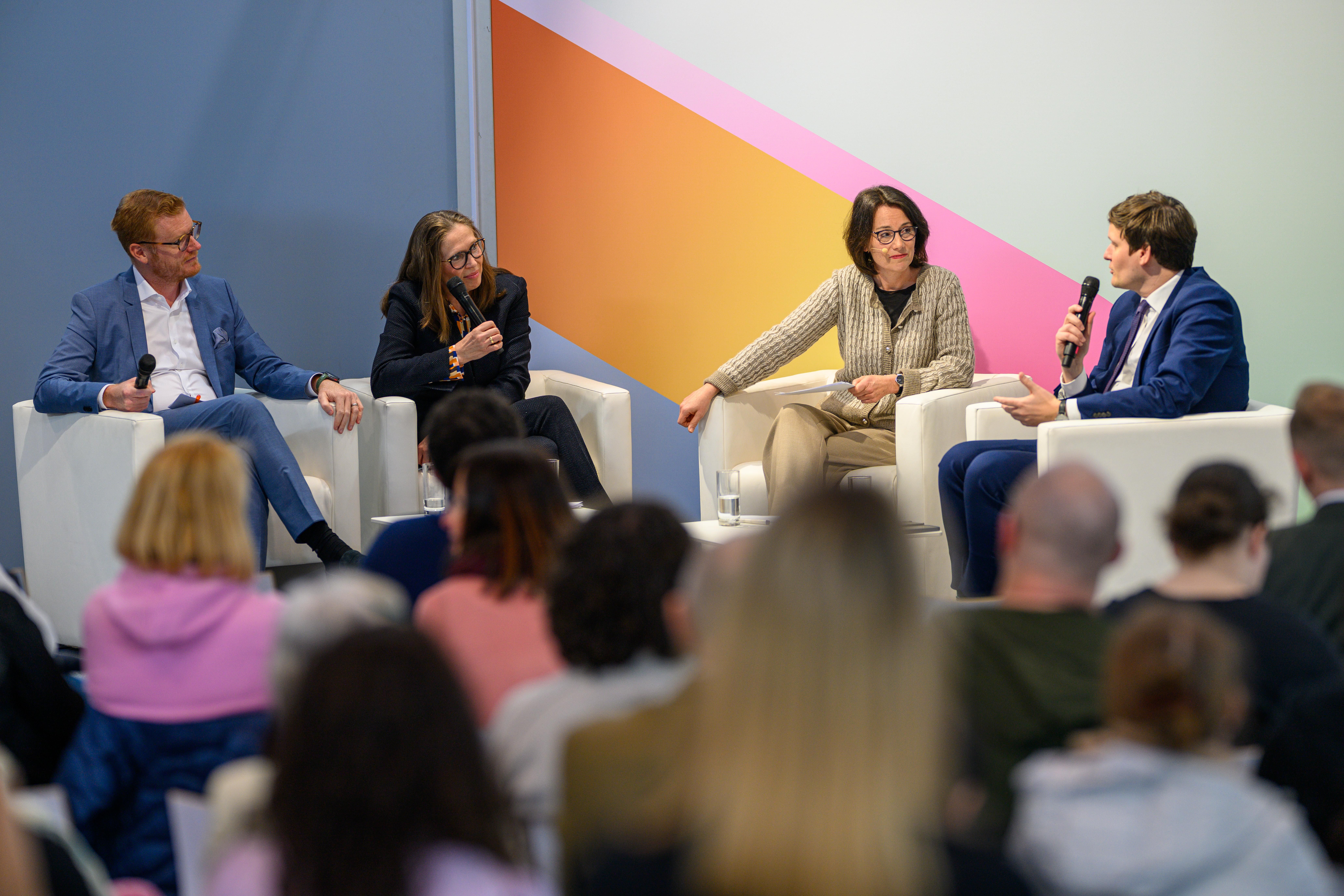 Conrad Clemens sitzt auf der Bühne in einem Podium und spricht ins Mikrofon