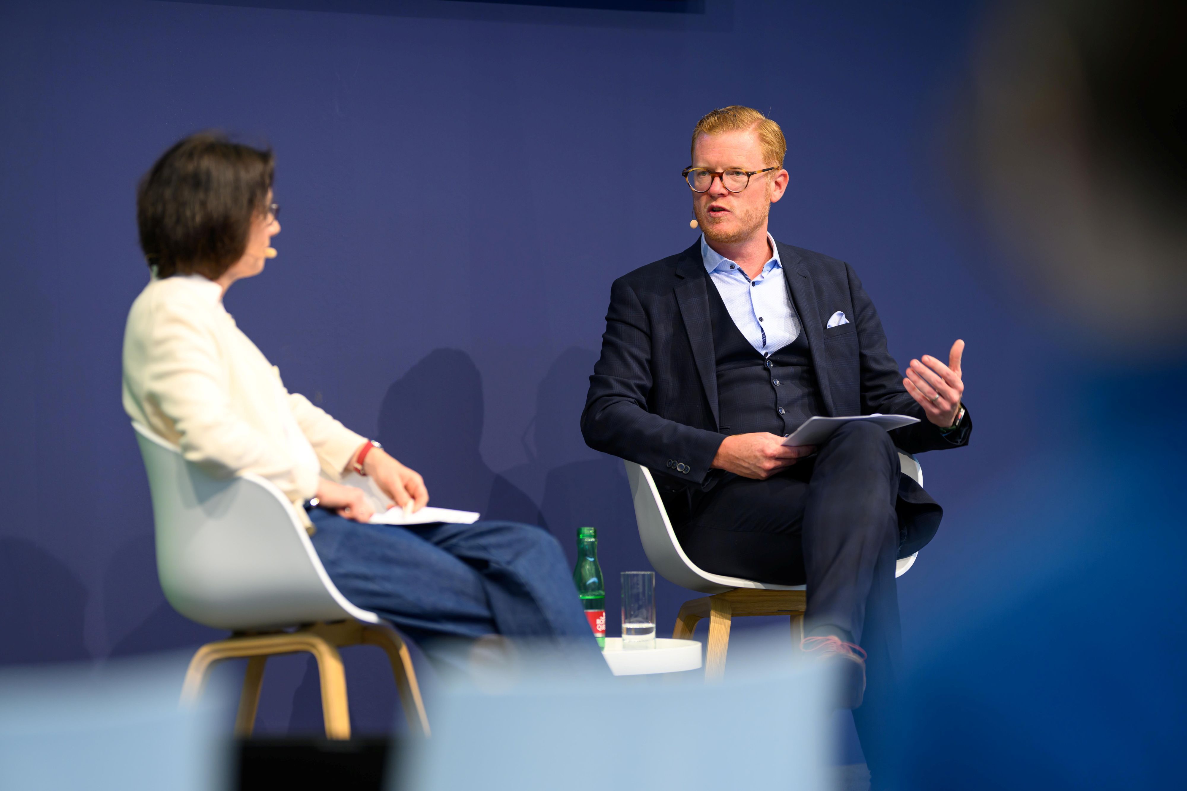 Maximilian Schulyok sitzt auf der Bühne und spricht mit Katja Irle