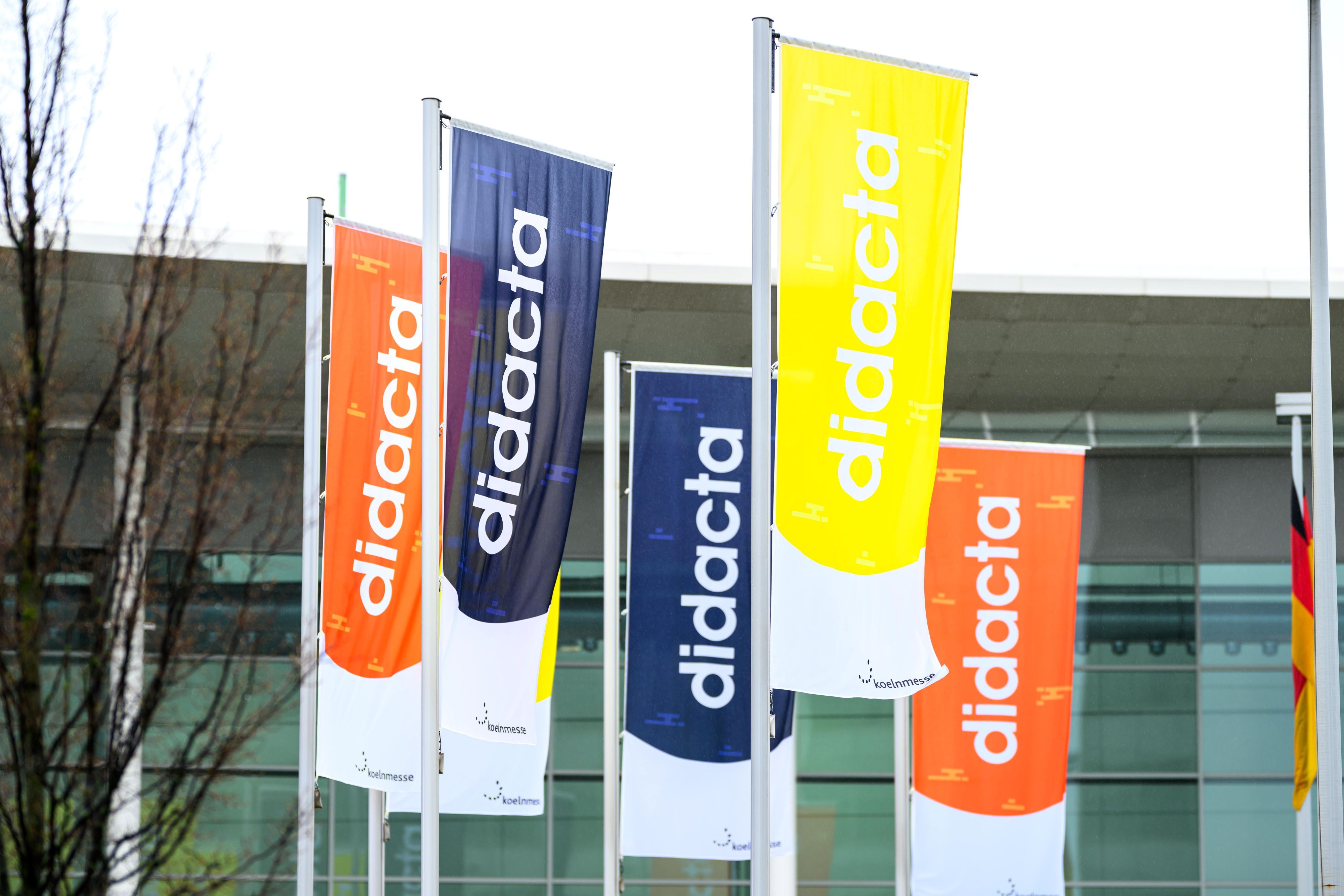 Bunte Fahnen mit dem didacta-Logo wehen vor der Koelnmesse im Wind.