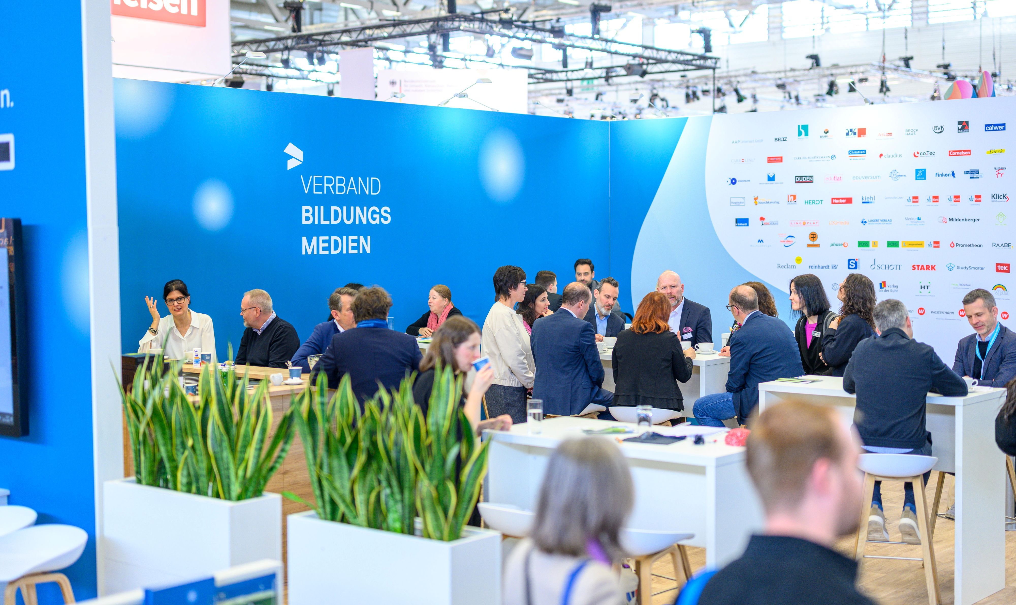 Menschen sitzen und stehen auf dem Messestand des Verband Bildungsmedien