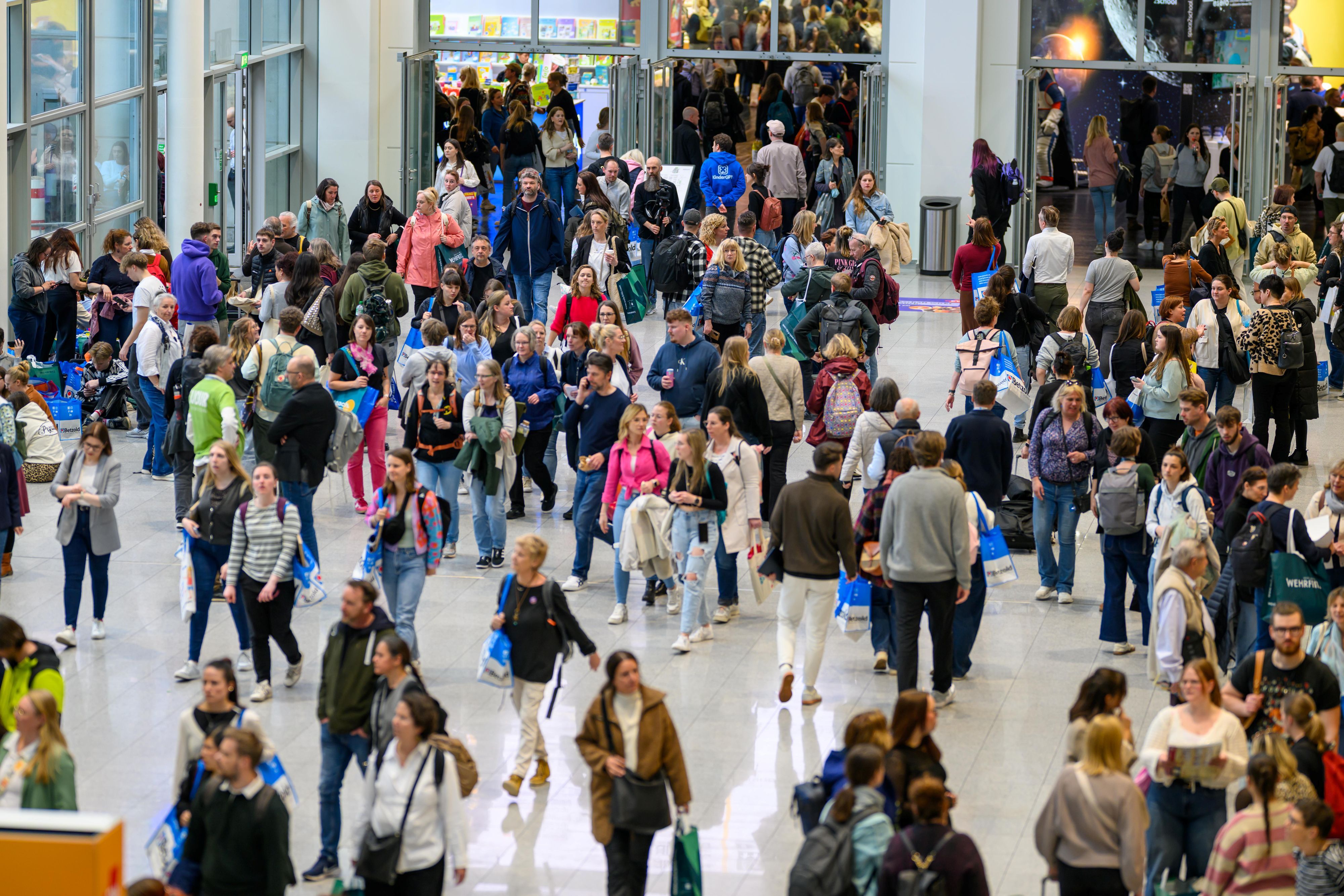 Menschen laufen durch eine Eingangshalle der Koelnmesse