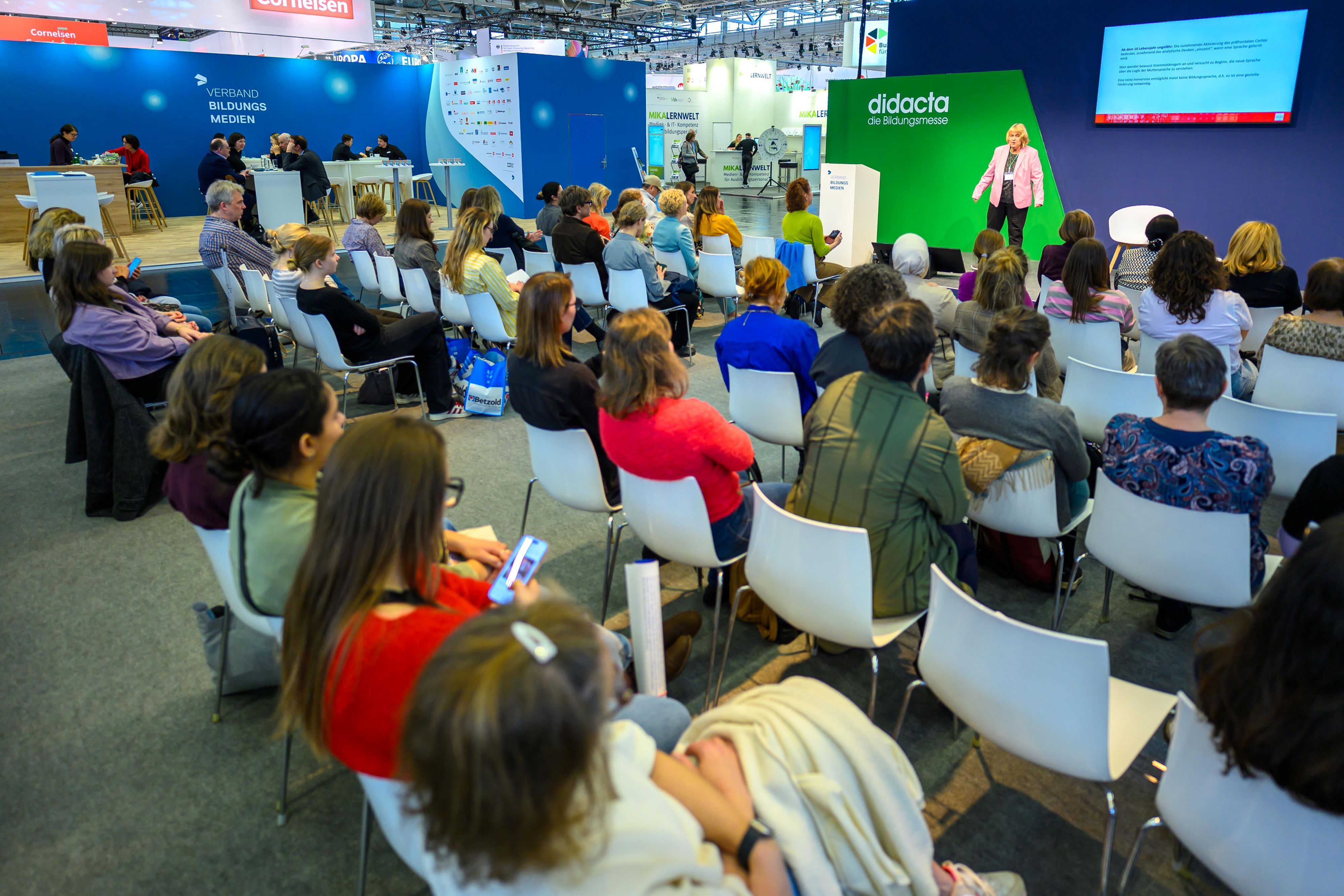 Besucherinnen und Besucher sitzen auf Stühlen und schauen zur Bühne