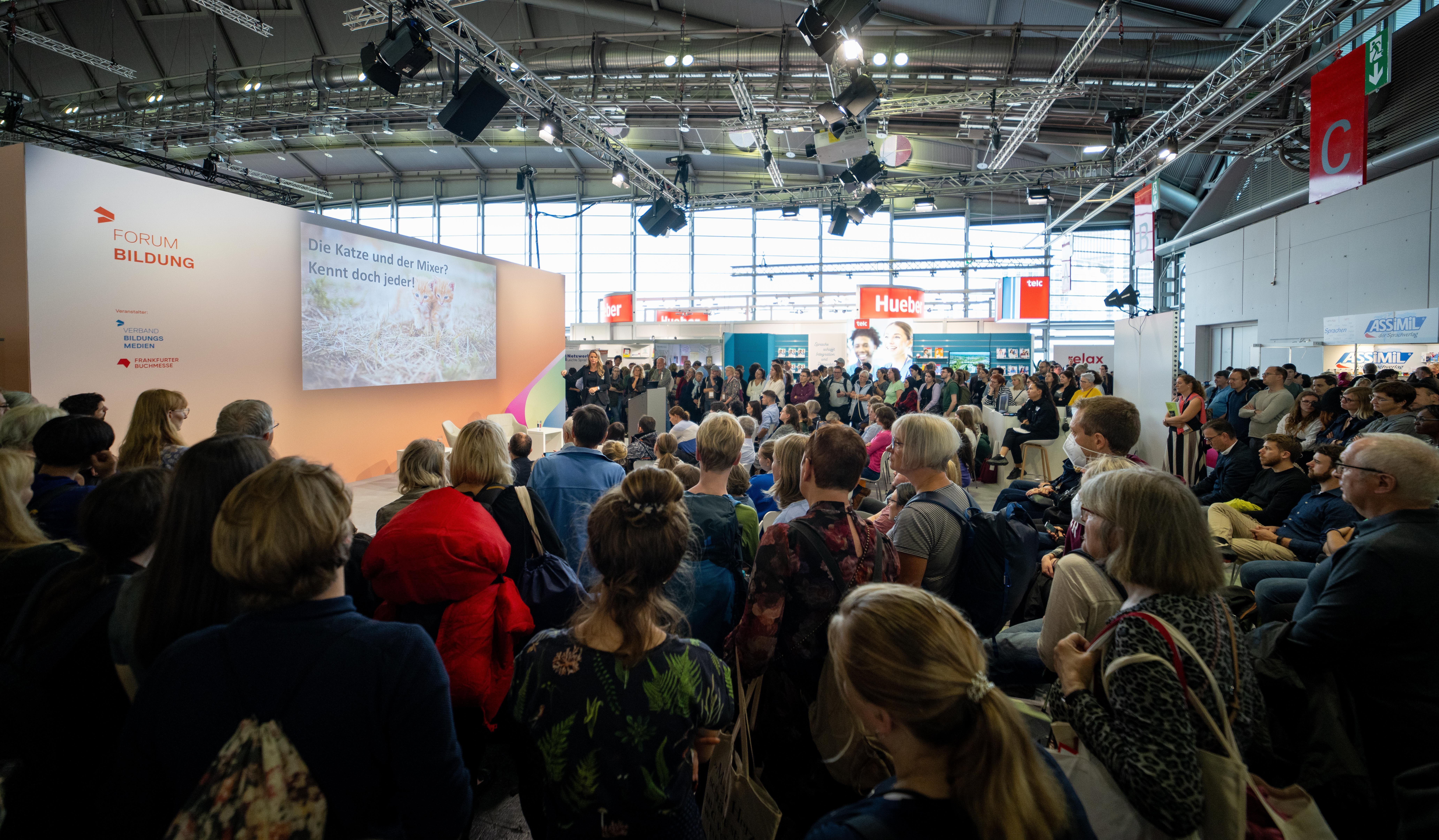 150 Menschen stehen um die Bühne des Forum Bildung herum und hören Silke Müller zu.